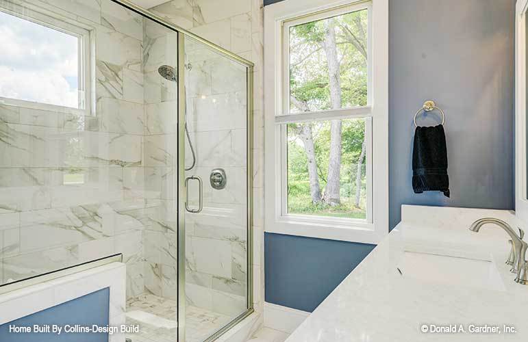 Primary bathroom with a marble top vanity, a walk-in shower, and a white framed window that allows natural light in.