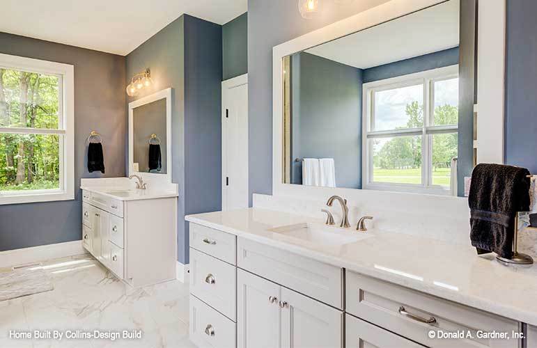 His and her sink vanities with white cabinets, large mirrors, and warm glass sconces.