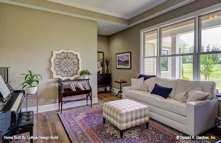 Sitting room with an upright piano and a beige sectional paired with a checkered ottoman.