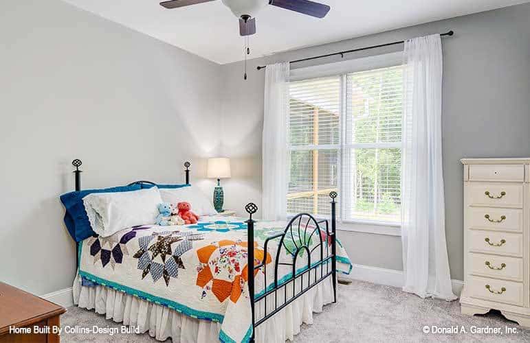 Another bedroom with carpet flooring, a wrought iron bed, and a large window dressed in white sheer curtains.