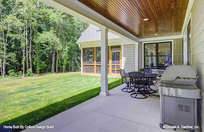 The rear porch is filled with an outdoor dining set and a barbecue grill over concrete flooring.