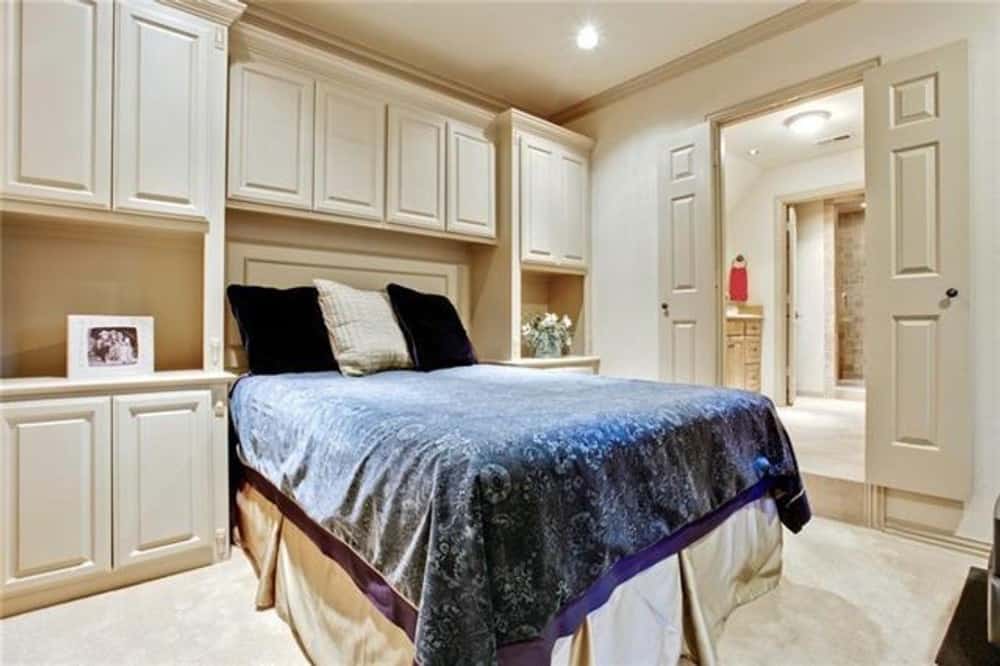 Primary bedroom with white built-ins and a skirted bed over the carpet flooring. A double door on the side leads to the primary bath.