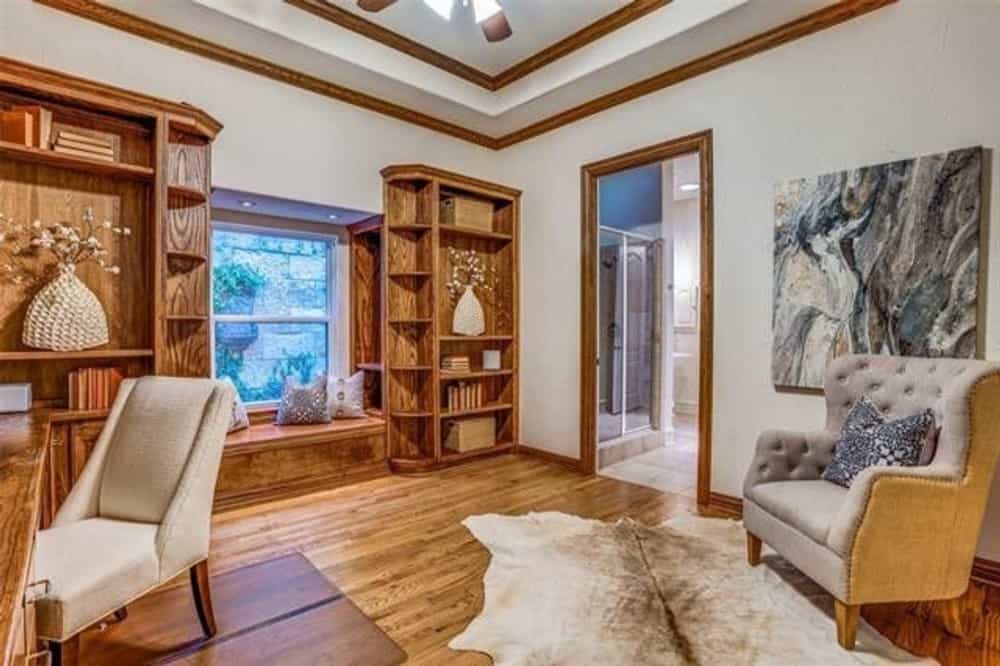 Study with a tray ceiling, a wooden desk, upholstered chairs, and a window seat flanked by built-in shelves.