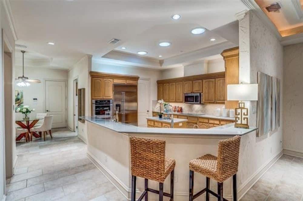 The kitchen is equipped with wooden cabinetry, stainless steel appliances, a small center island, and an angled peninsula paired with wicker counter chairs.