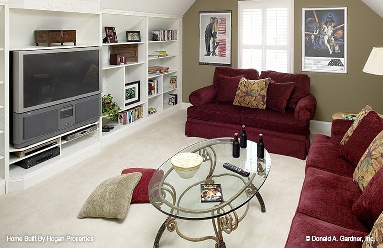 The bonus room has a vaulted ceiling, carpet flooring, red sofas, and white built-ins.