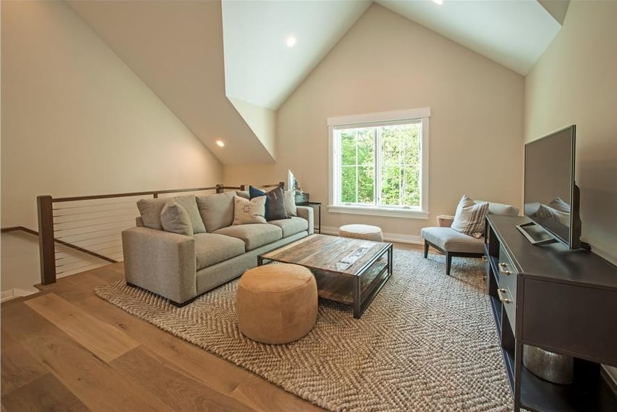 Loft area with a gray sectional, cushioned chair, a TV, and round ottomans flanking the rustic coffee table.