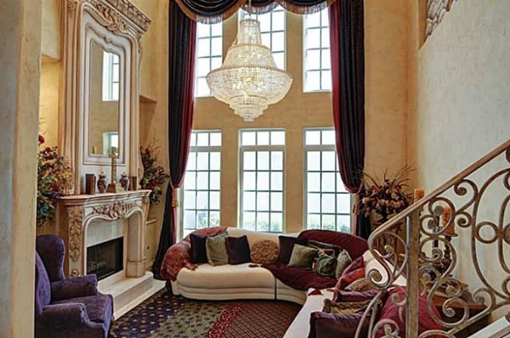 Living room with an ornate fireplace, classy sofas, and clerestory windows dressed in red drapes and valances.