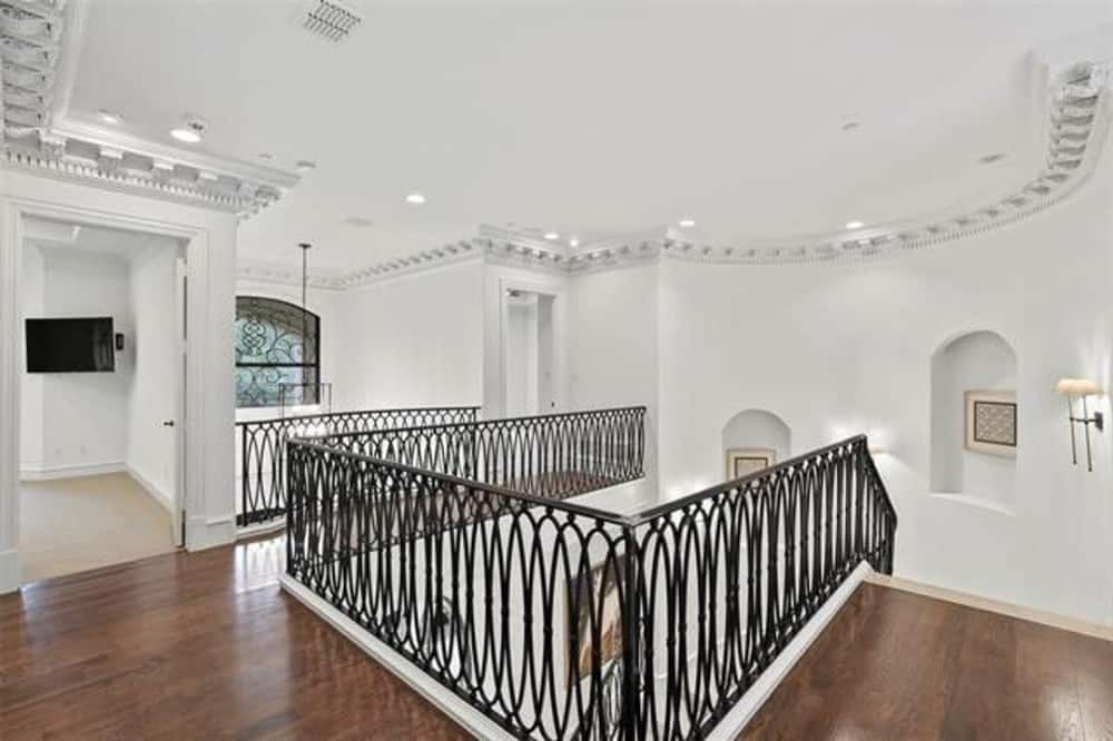 Second-level balcony with hardwood flooring, arched niches, and wrought iron railings.
