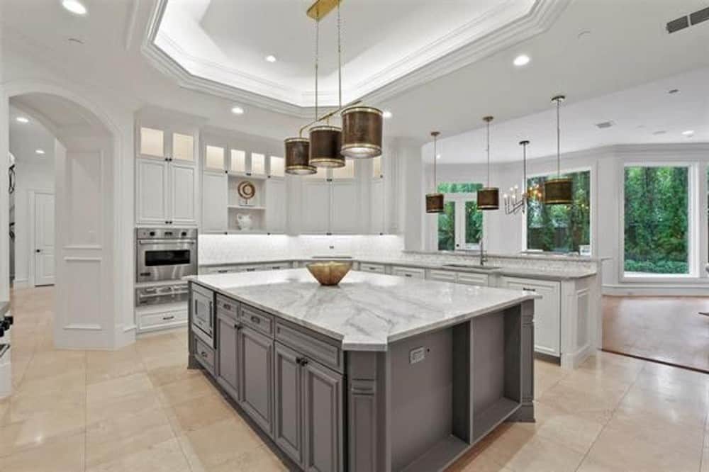 The kitchen is equipped with stainless steel appliances, white cabinetry, and a large center island highlighted by a tray ceiling.