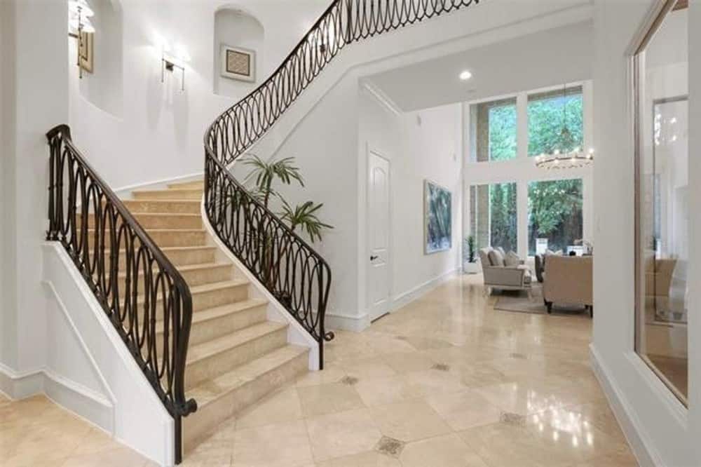 Foyer with marble tile flooring and a winding staircase framed with ornate wrought iron railings.