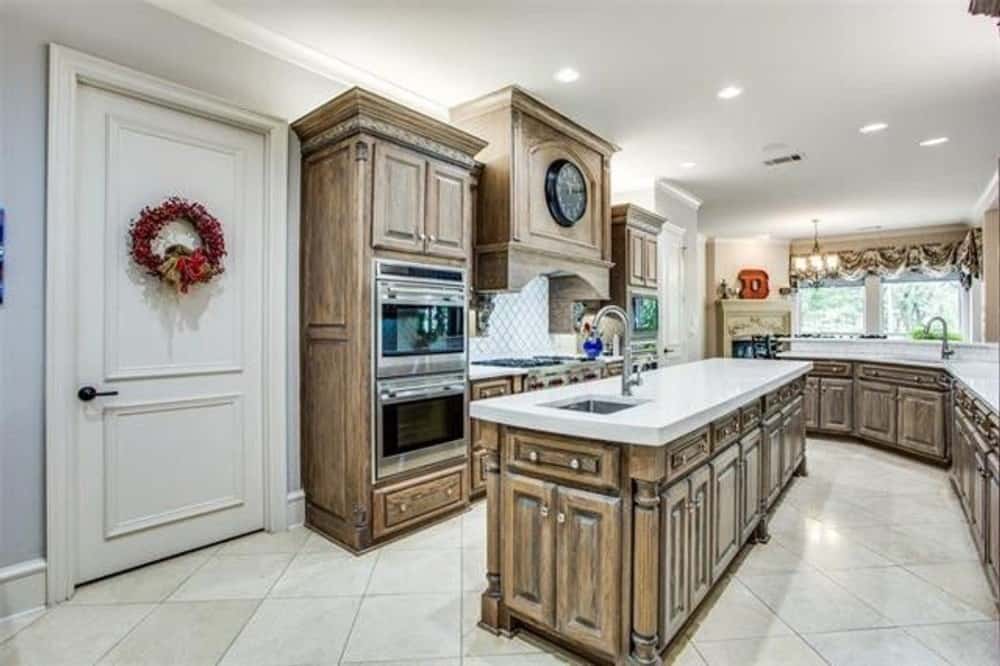 Kitchen with natural wood cabinetry, marble countertops, and a large island fitted with a sink.