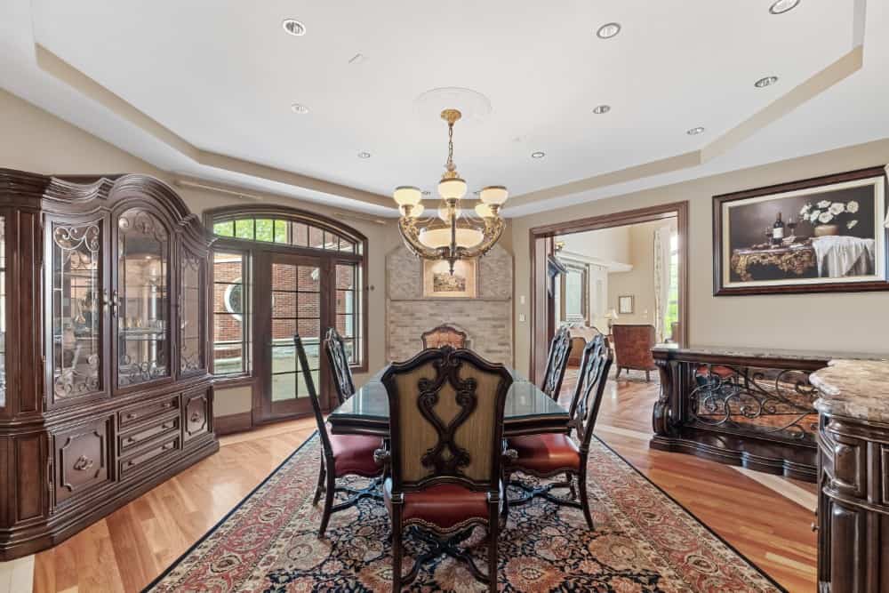 Formal dining room with a tray ceiling, a 6-seater dining set, and matching china cabinet and buffet table graced with intricate detailing. Image courtesy of Toptenrealestatedeals.com.