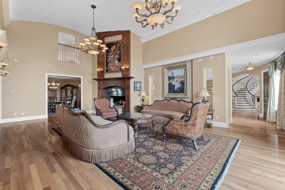 The living room has beige walls, a corner fireplace, vintage-style seats, and light hardwood flooring topped with a tasseled area rug. Image courtesy of Toptenrealestatedeals.com.