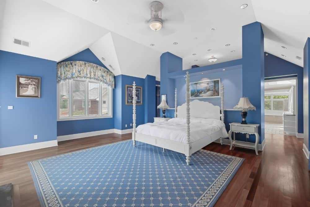 Bedroom with a white vaulted ceiling, a four-poster bed, and a patterned area rug that matches with the blue walls. Image courtesy of Toptenrealestatedeals.com.