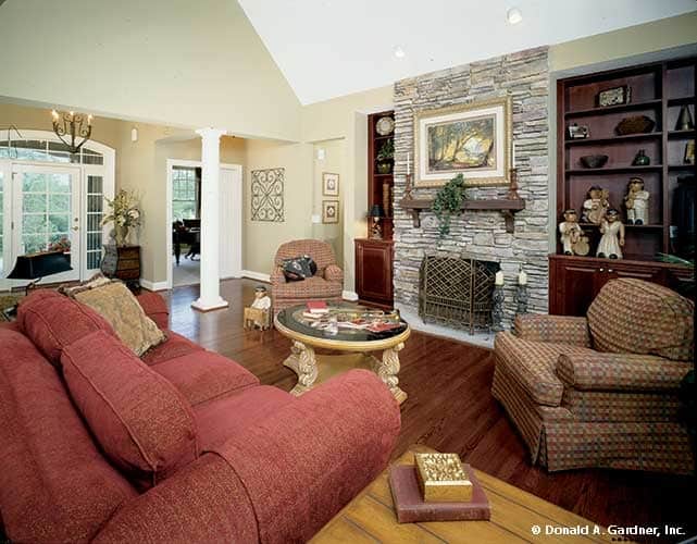 The great room offers a stone fireplace, patterned armchairs, and a large, red sofa paired with a round coffee table.