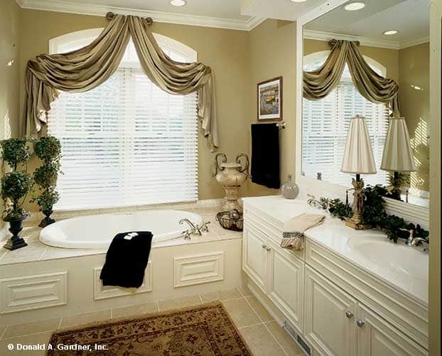 The primary bathroom boasts a dual sink vanity and a deep soaking tub graced with a decorative vase and classy valances.