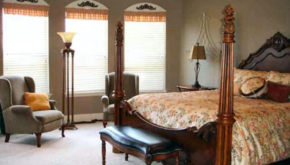 The primary bedroom has a four-poster bed, a leather cushioned bench, and a sitting area by the bow window.