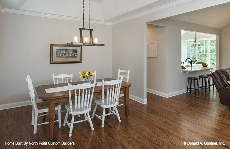 The formal dining room offers white chairs and a wooden dining table well-lit by a linear chandelier.