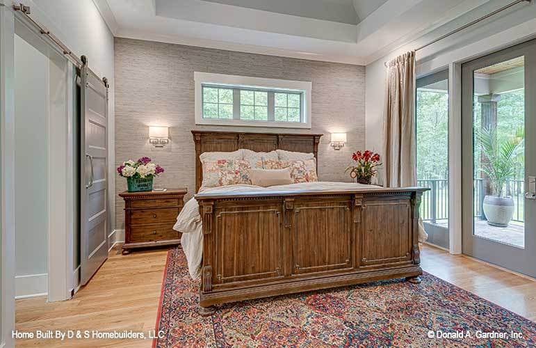 Primary bedroom with a tray ceiling, natural wood furnishings, and a private porch accessible through a glazed door.