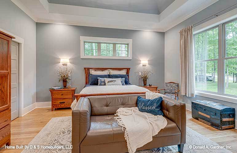 This bedroom has gray walls, a trunk storage chest, and a wooden bed complemented with a leather tufted loveseat.