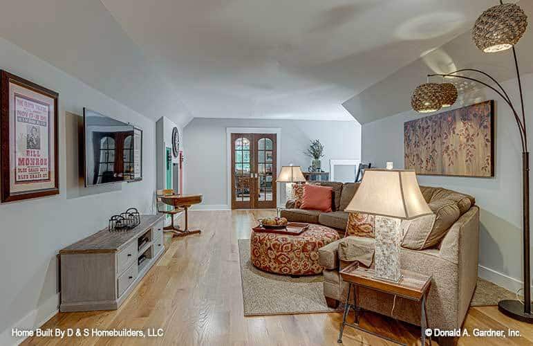 The bonus room includes a living space furnished with a rustic TV stand, a curved sectional, and a round patterned ottoman.
