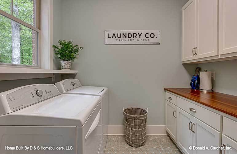 The laundry room is filled with top-load appliances, a perforated hamper, white cabinets, and a wooden countertop.