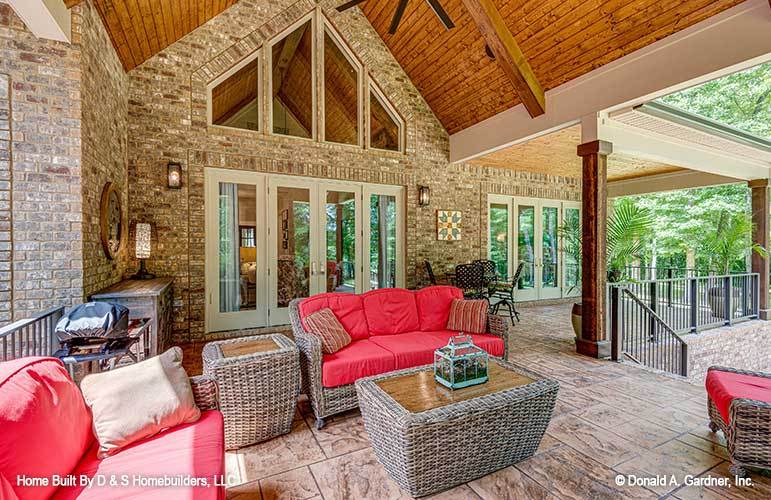 Screened porch with a cathedral ceiling, wicker tables, and matching seats accented with red cushions.