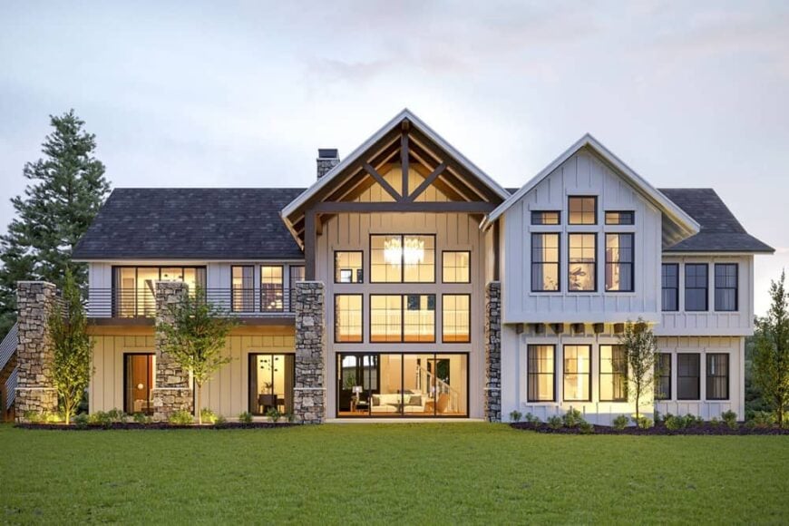 Rear exterior view showing the board and batten siding, covered porch, upper deck, and plenty of large windows highlighted with ambient lighting.
