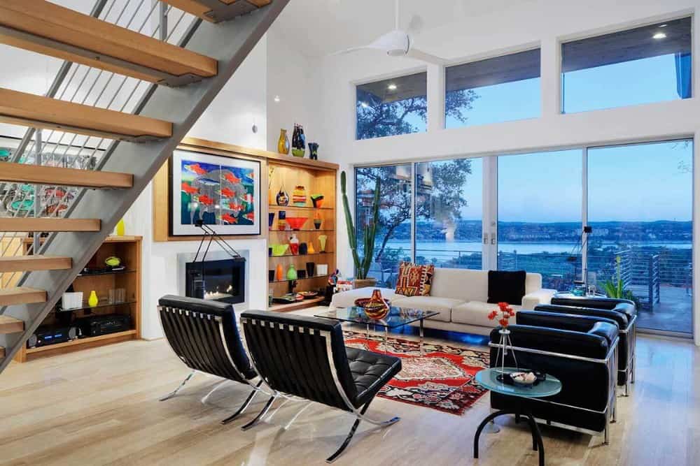Great room with a modern fireplace, built-in shelves, a gray sectional, leather chairs, clerestory windows, and sliding glass doors leading to the rear deck.