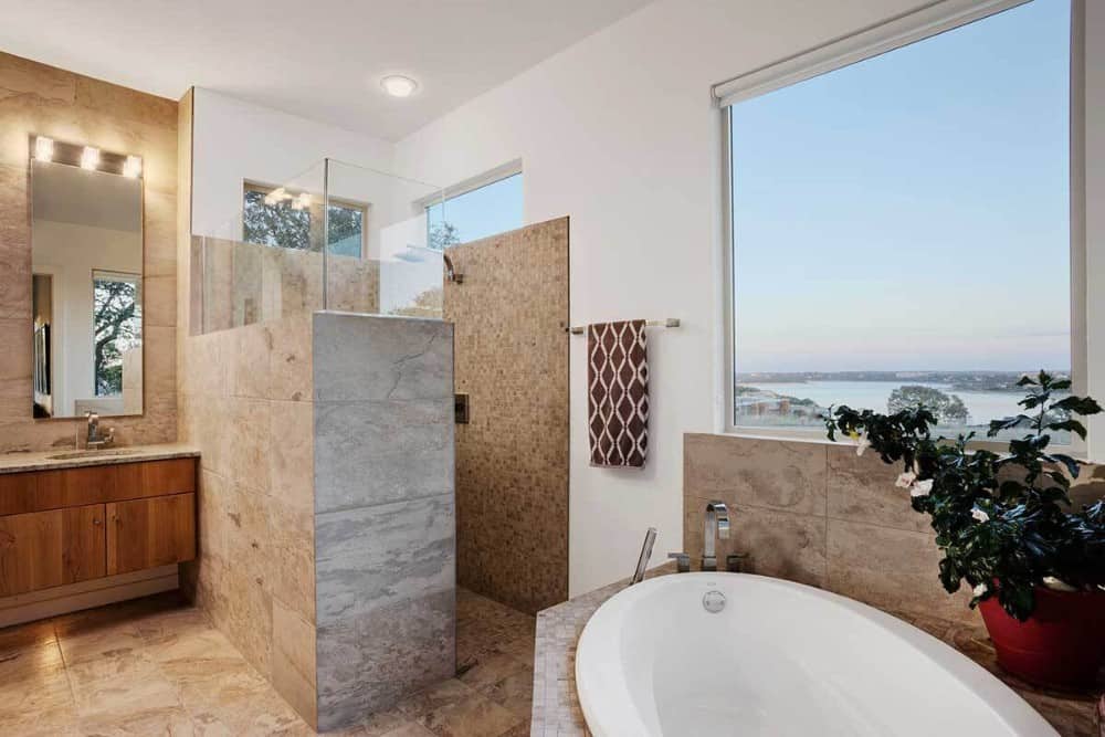 Primary bathroom with a wooden vanity, a walk-in shower, and a corner tub placed under the picture window overlooking a breathtaking view.