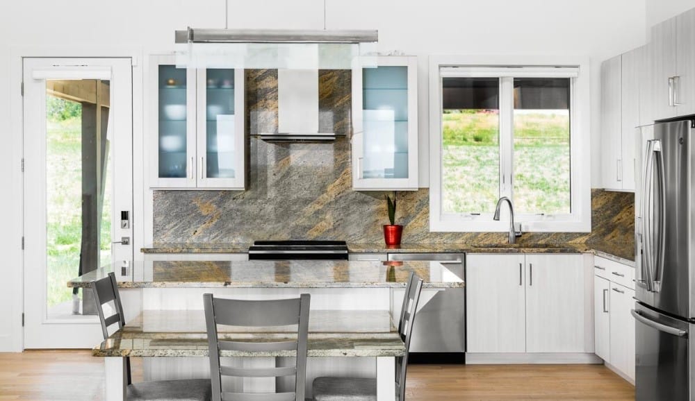 Kitchen with white and glass-front cabinetry, stainless steel appliances, and a granite top island integrated with an eating bar.