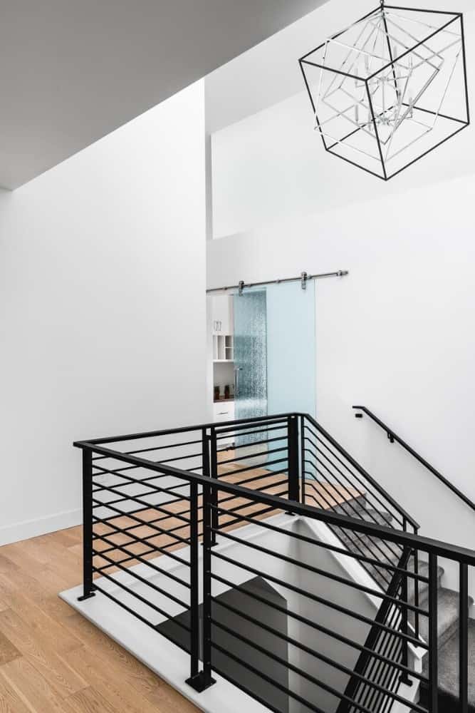 Hallway with hardwood flooring and wrought iron railings illuminated by an oversized geometric pendant.