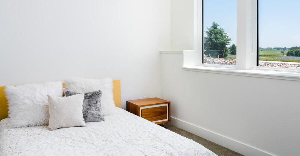 This bedroom has stark white walls and a comfy bed filled with furry pillows.