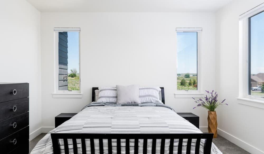 Another bedroom with pristine white walls, dark wood furnishings, and plenty of windows that invite natural light in.