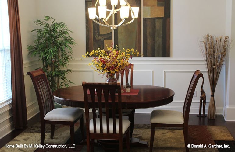 The dining room has white wainscoted walls and a round dining set well-lit by a spherical chandelier.