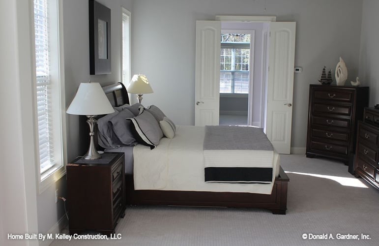 Primary bedroom with dark wood furnishings, carpet flooring, and a french door leading to the ensuite.