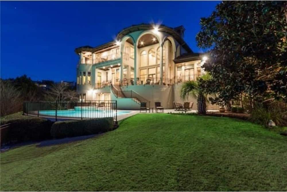View of the house from the backyard showing its covered verandas, upper balconies, and a pool terrace furnished with tufted lounge chairs.