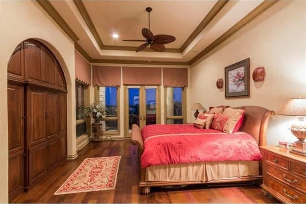Primary bedroom with a classy wooden bed, a red patterned runner, and a ceiling fan fixed on a tray ceiling bordered by wooden moldings.