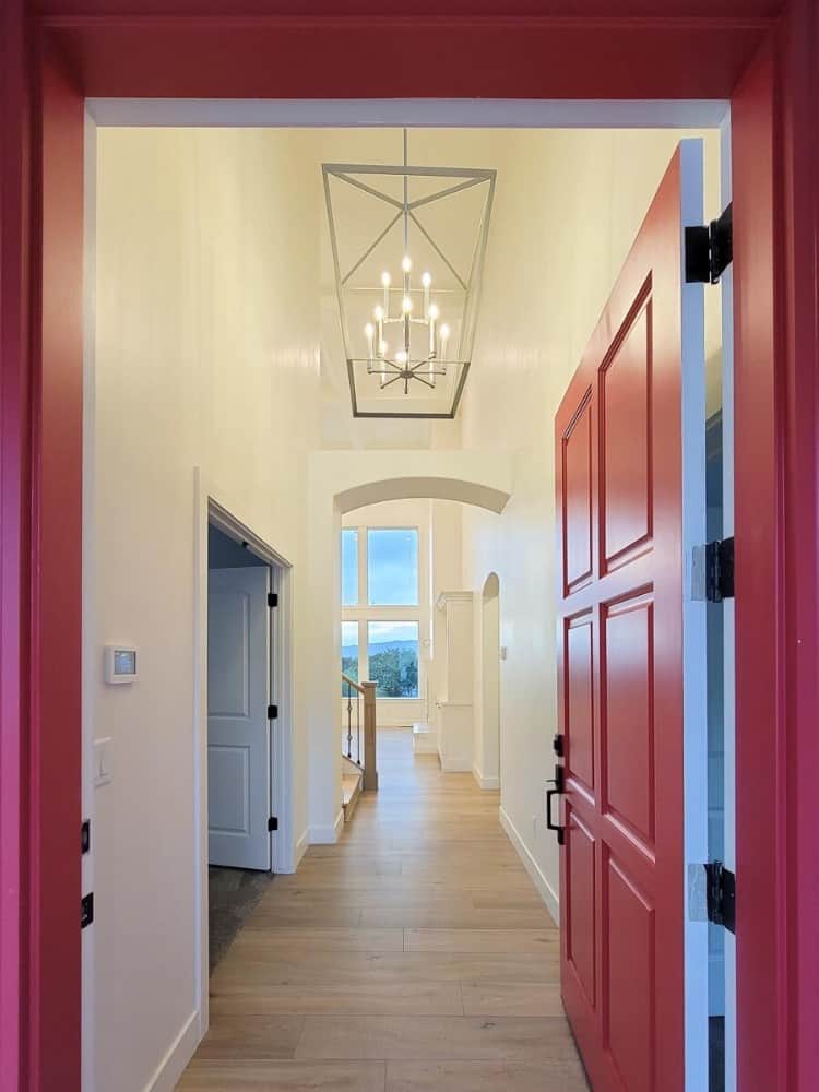 The red front door opens into the entryway crowned with a two-story ceiling. It has a large caged chandelier and an open archway leading to the living space.