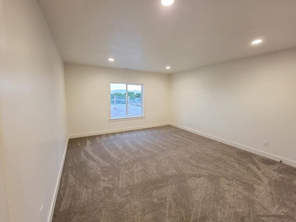Another bedroom with carpet flooring, recessed ceiling lights, and white walls lined with base moldings.