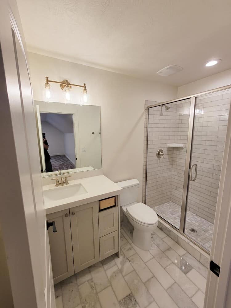 This bathroom is equipped with a sink vanity, a toilet, and a walk-in shower enclosed in a sliding glass door.