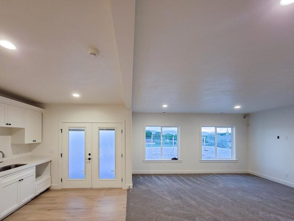 Lower-level family room carpet flooring, recessed ceiling lights, and a nearby french door that opens onto the rear patio.