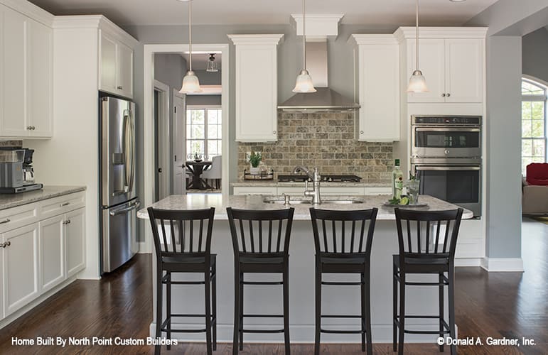 Kitchen with white cabinetry, stainless steel appliances, stone brick backsplash, and a breakfast island paired with dark wood counter chairs.
