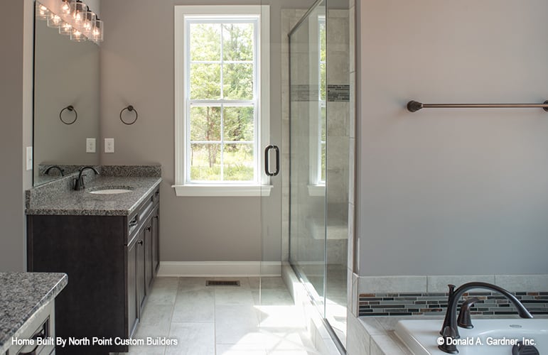 The primary bathroom is equipped with a drop-in bathtub, his and her sink vanities, and a walk-in shower enclosed in a hinged glass door.