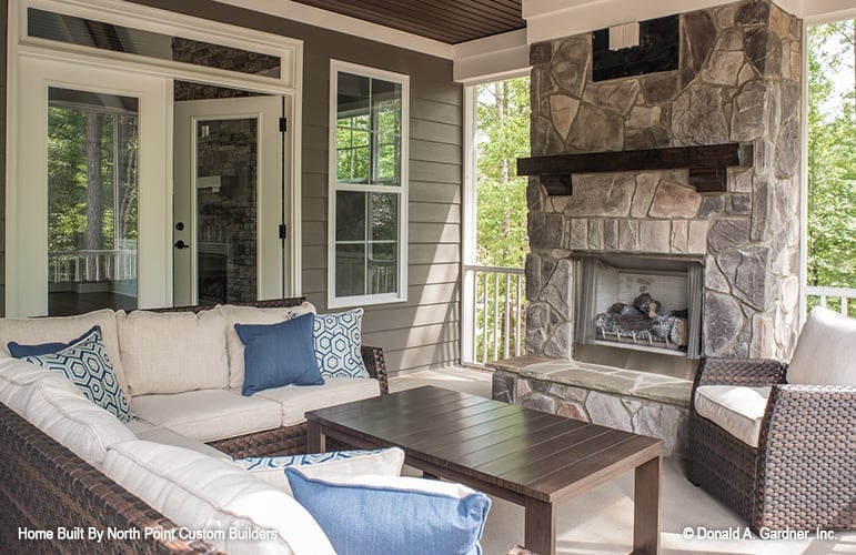 Screened porch with a stone fireplace and wicker cushioned seats surrounding the wood plank coffee table.