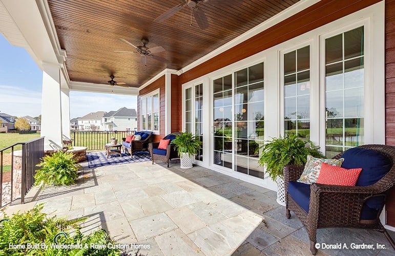 Covered porch with limestone flooring, cushioned wicker seats, and a wood-paneled ceiling mounted with ceiling fans.Covered porch with limestone flooring, cushioned wicker seats, and a wood-paneled ceiling mounted with ceiling fans.