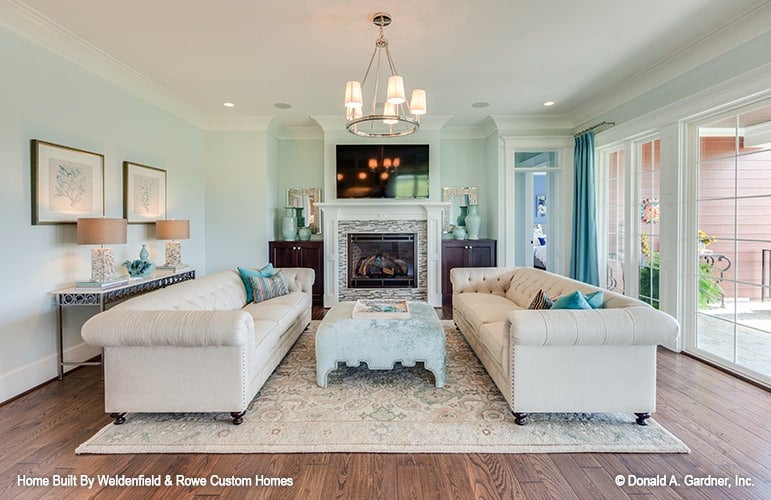 Great room with facing Chesterfield sofas, a contemporary ottoman, and a fireplace topped with a TV.