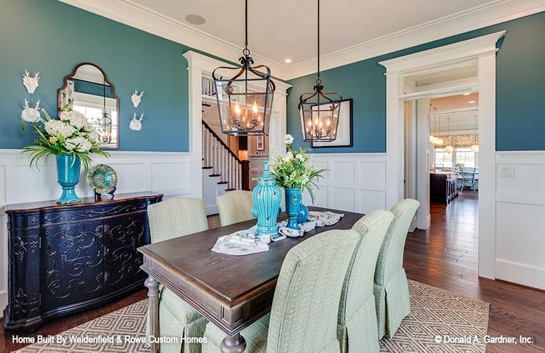 Dining room with a couple of iron pendants, a wooden dining table, skirted chairs, and a carved wood buffet table paired with an arched mirror.