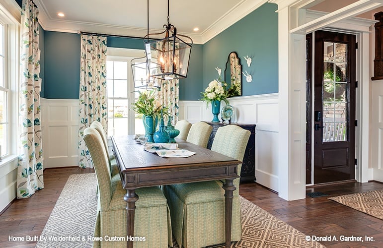 The dining room is adorned with white wainscoting and patterned drapes accentuating the white-framed windows.