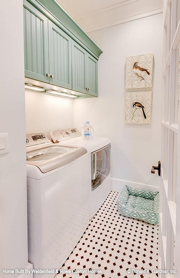 Utility room with tiled flooring, sage green overhead cabinets, white washer and dryer, and a couple of bird artworks gracing the stark white walls.